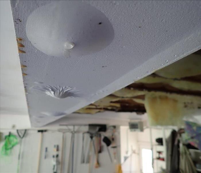 Water pockets behind painted drywall and ceiling fallen in in garage due to a cracked toilet