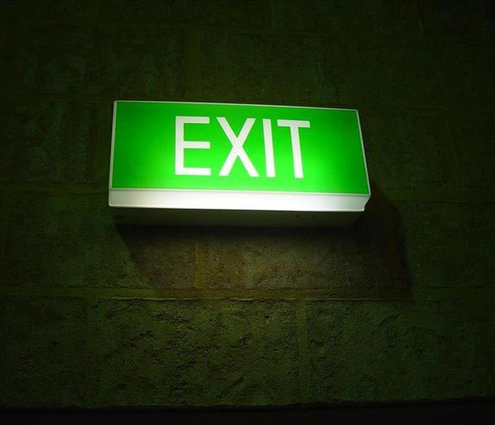 Green lighted exit sign hanging on cement block wall